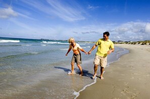 Escena de playa con dos personas caminando por la orilla.