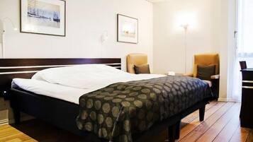 Una habitación de hotel con una cama, dos sillas, un escritorio y dos cuadros en la pared.