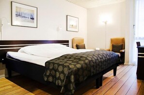 Una habitación de hotel con una cama, dos sillas, un escritorio y dos cuadros en la pared.