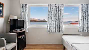 Ein Hotelzimmer mit einem Bett, einem Fernseher, einem Schreibtisch und einem Fenster mit Vorhängen.