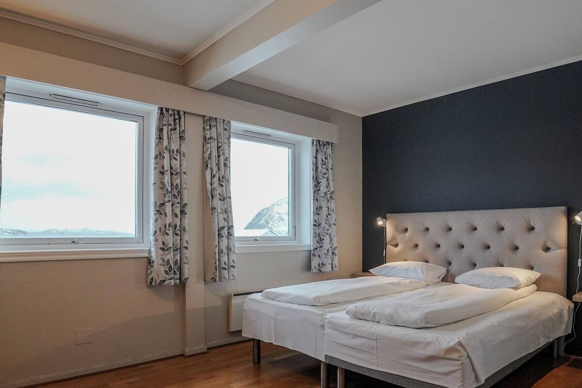 A bedroom with a large bed, a window with curtains, and a grey rug.