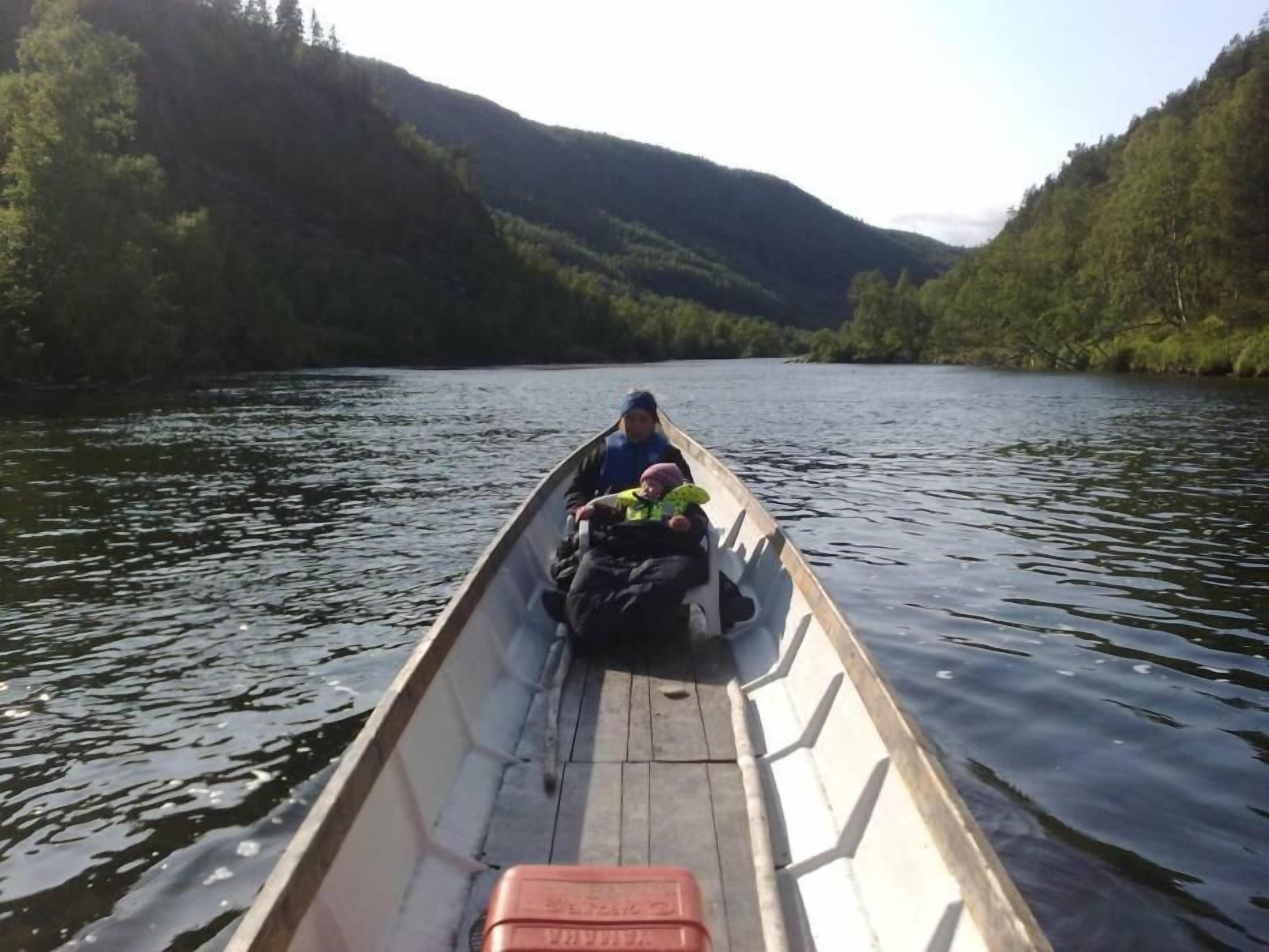 Un petit bateau navigue sur une rivière, entourée de collines boisées.
