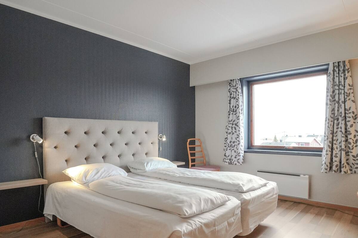 A bedroom with a large bed, a chair, a window with curtains, and a radiator.