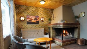 A cozy living room with a brick fireplace, a sofa, two armchairs, and a round wooden coffee table. - Reisafjord Hotel (Nordreisa)