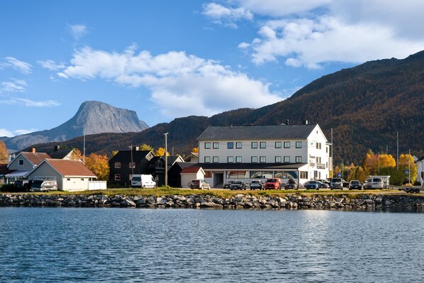 A coastal town with a prominent hotel featuring multiple floors, a parking area, and a backdrop of mountains. - Best Western Reisafjord Hotel (Nordreisa)