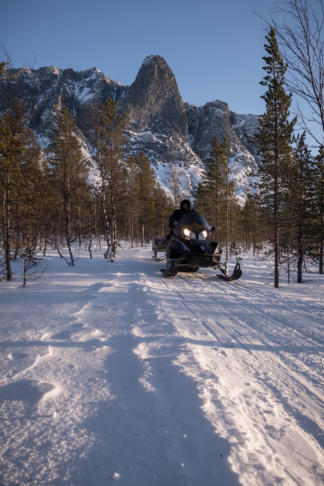 A snowmobile on a snowy path with a mountainous backdrop.