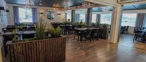 Ein geräumiges Restaurant mit Holzböden, schwarzen Stühlen und Kronleuchtern.