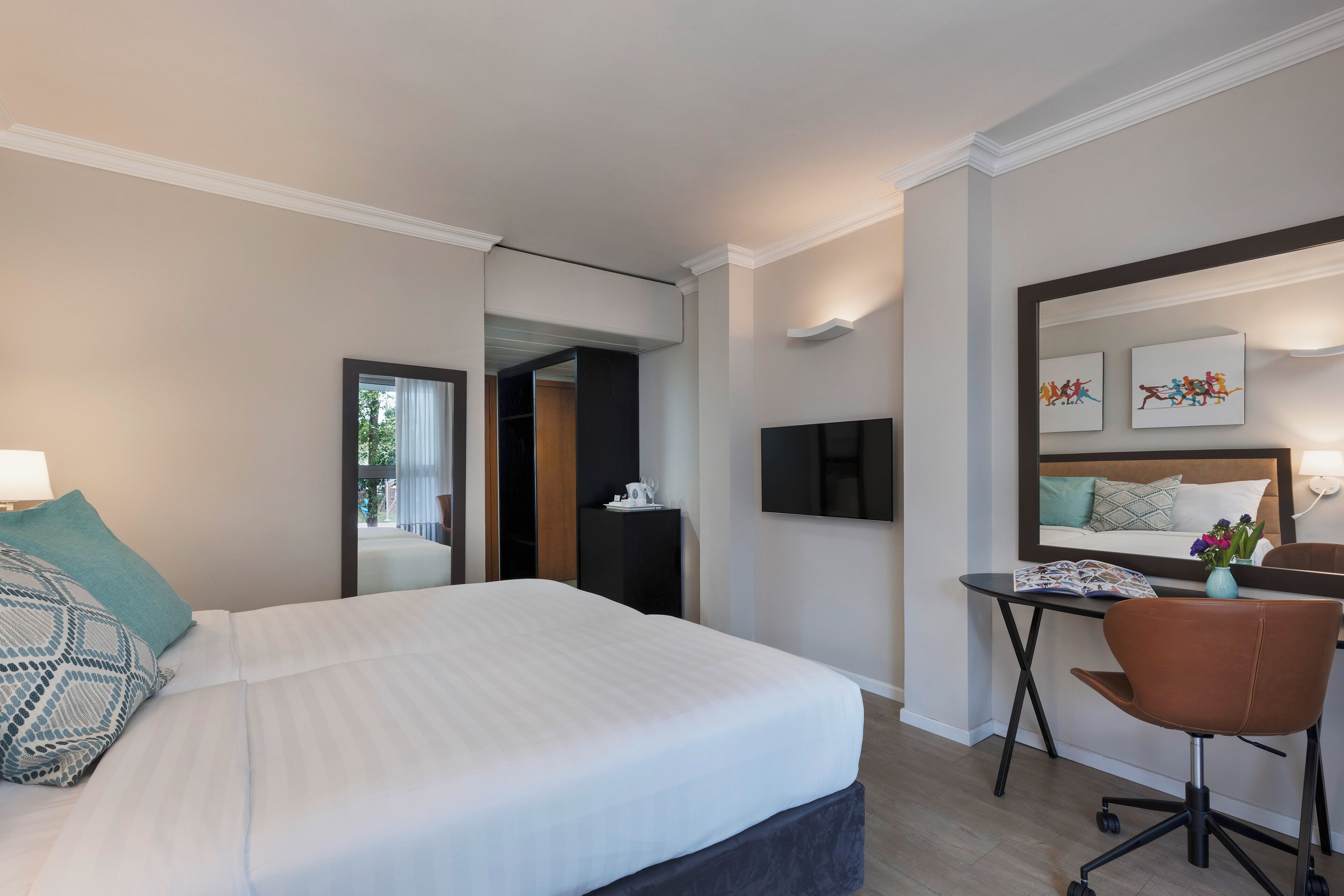 A hotel room with a large bed, a desk, a chair, and a mirror.