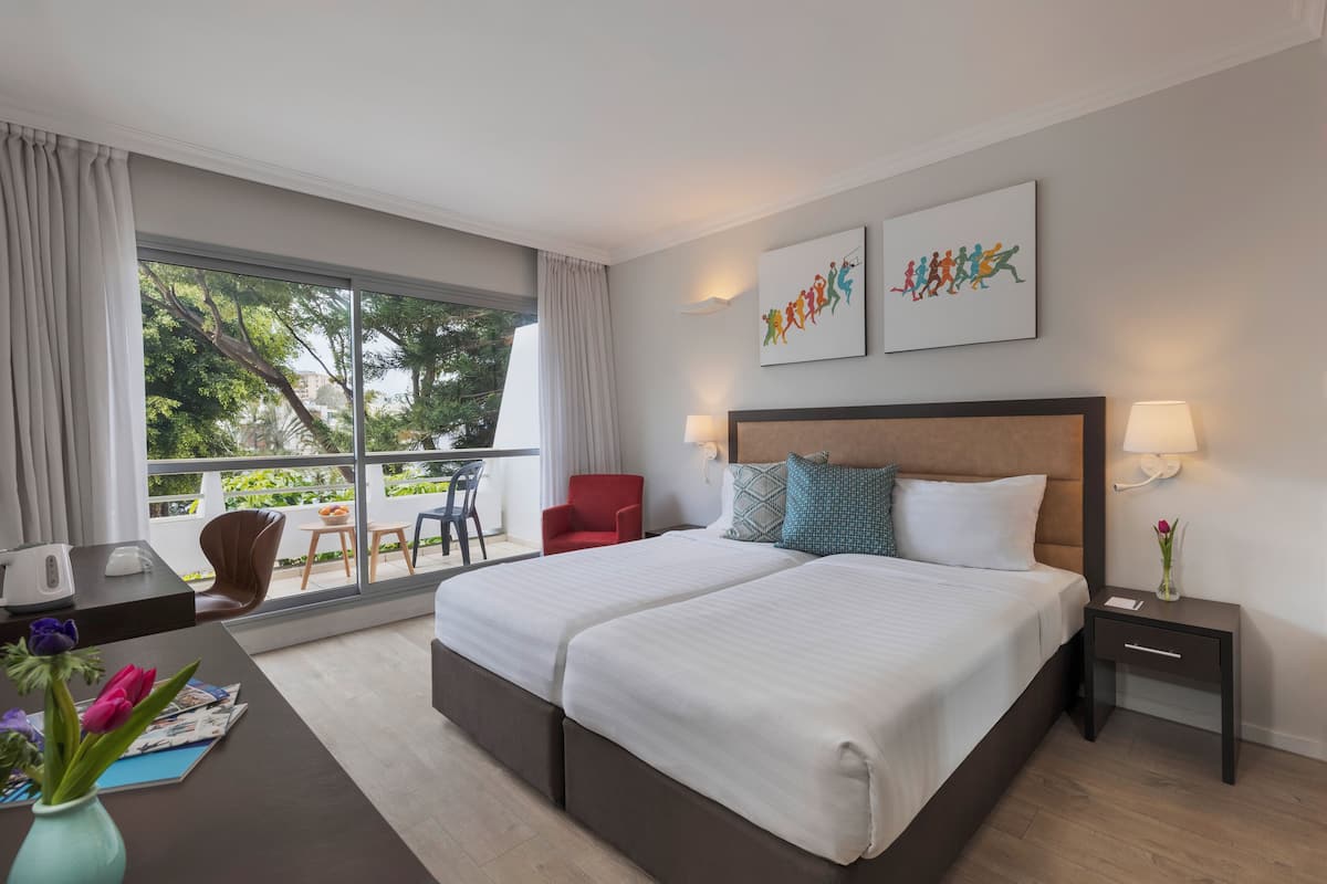 A hotel room with a large bed, a desk with a lamp, a chair, and a view of the outdoors.