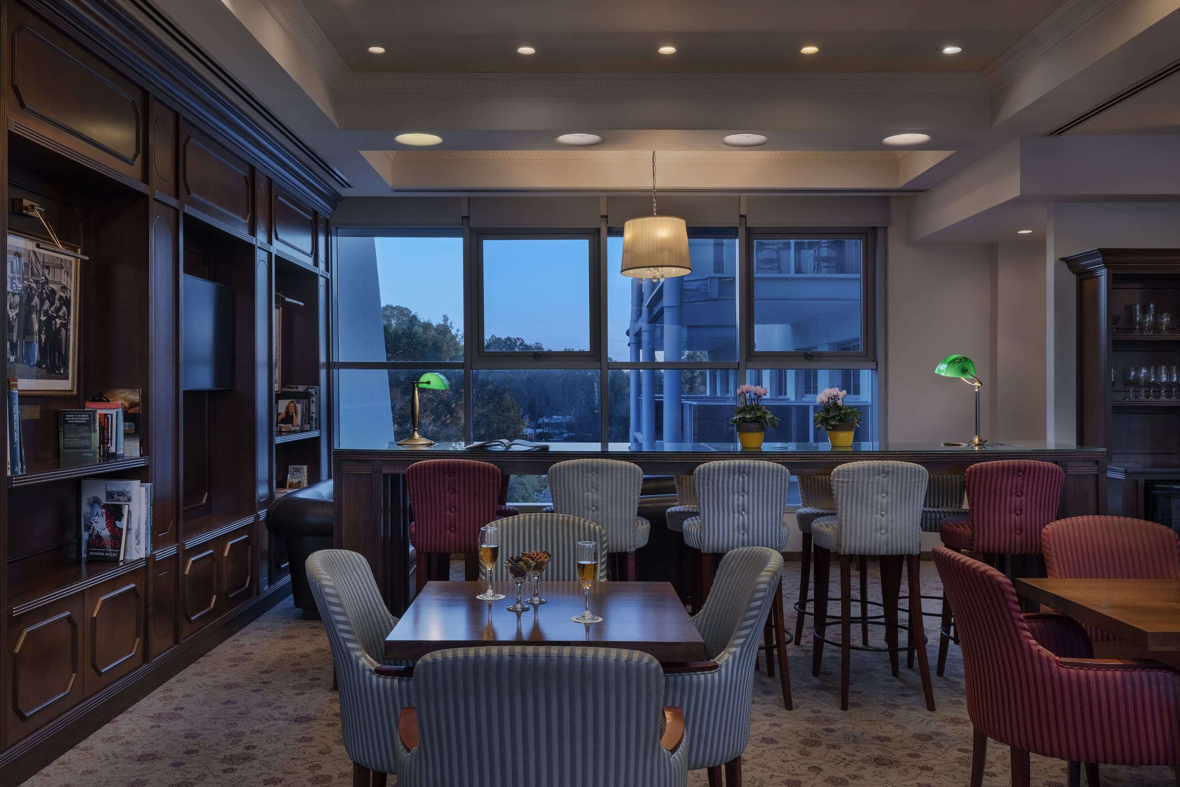 A dining area with a large window, multiple chairs, and a table set with glasses.