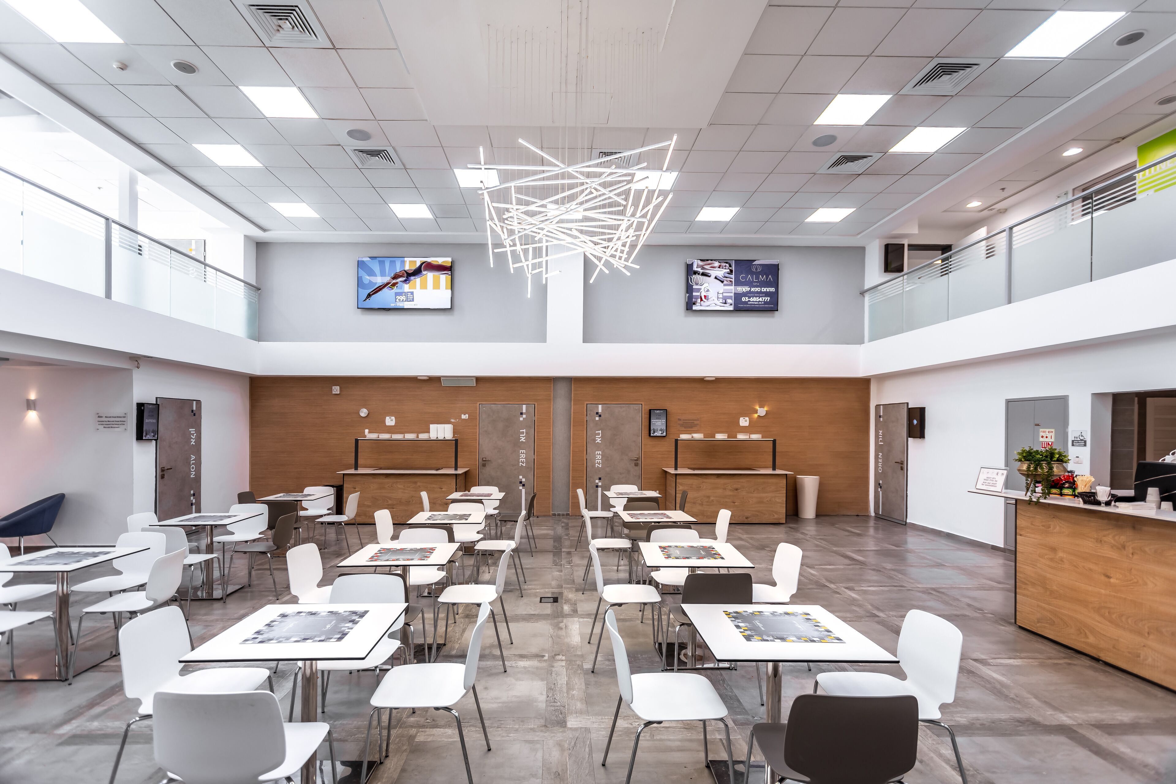 A modern conference room with white tables and chairs, a wooden reception desk, and a unique ceiling light fixture.