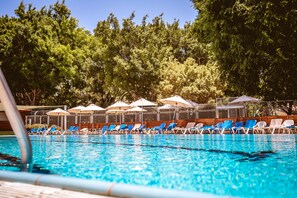 Une piscine entourée d’arbres, avec des chaises et des parasols bleus.