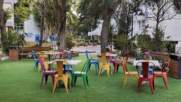 Un área de estar al aire libre con sillas y mesas coloridas, rodeada de follaje y árboles.