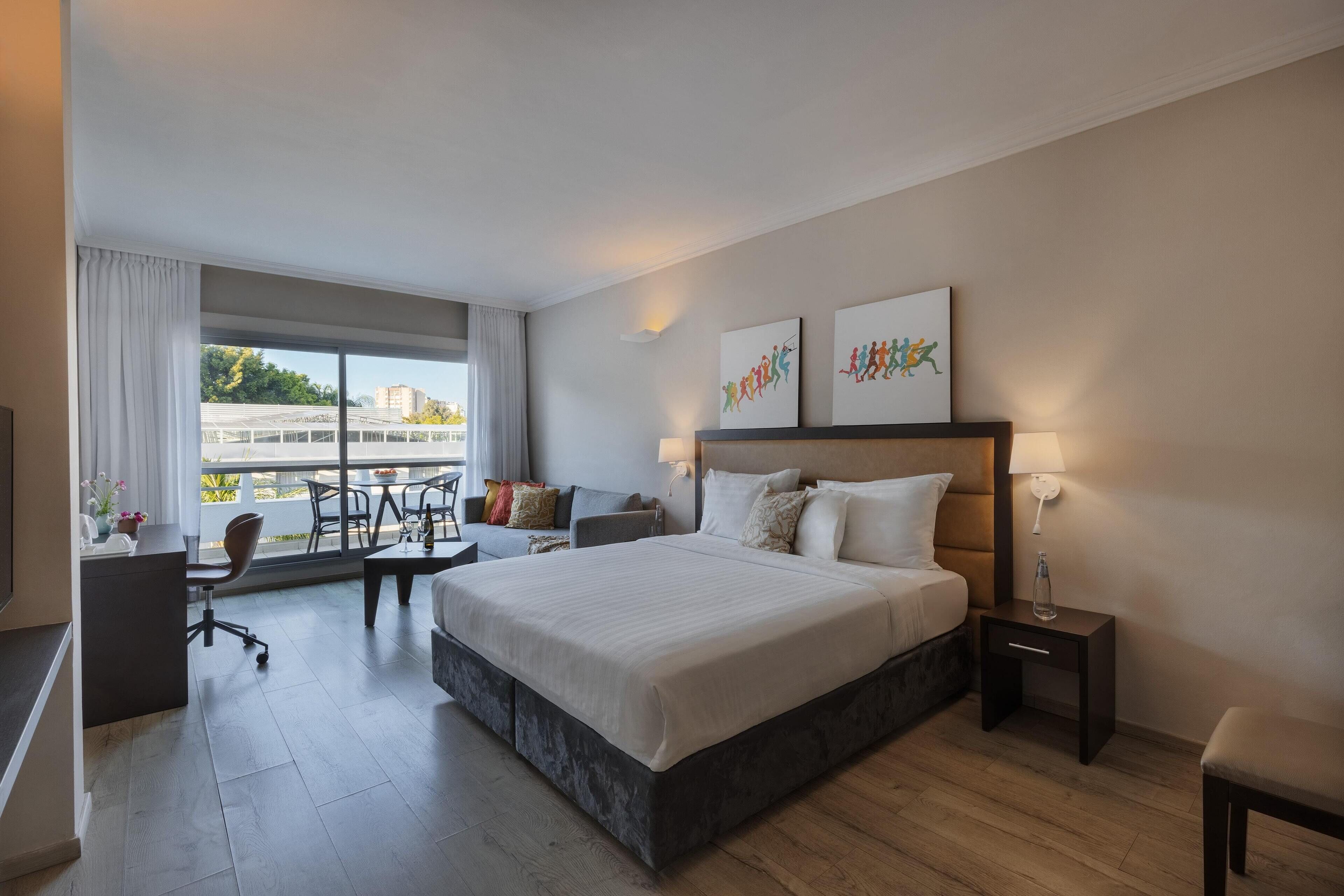 Ein modernes Hotelzimmer mit einem großen Bett, einem Schreibtisch, einem Sessel und Blick auf die Stadt.