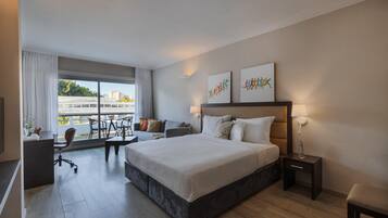Ein modernes Hotelzimmer mit einem großen Bett, einem Schreibtisch, einem Sessel und Blick auf die Stadt.