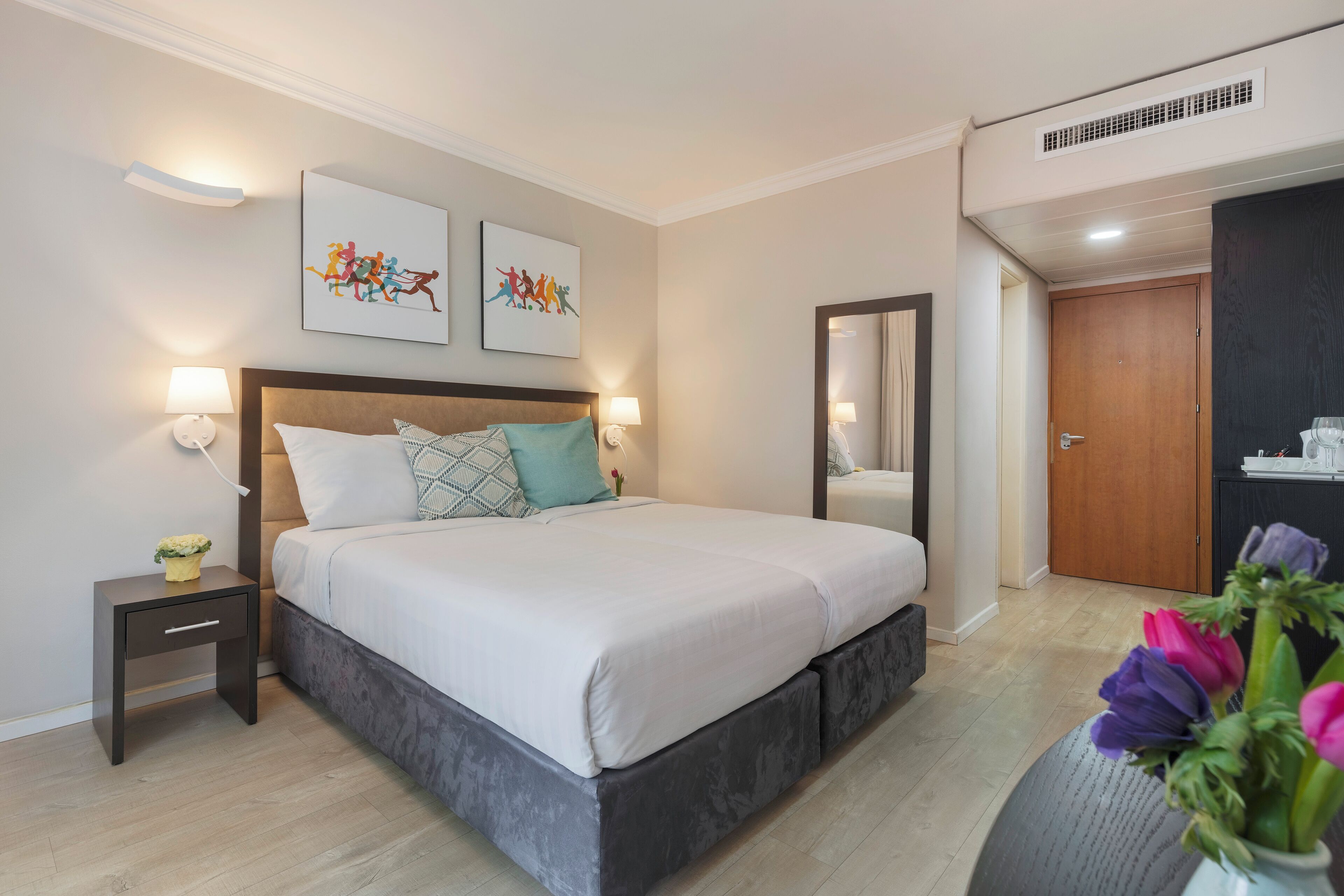 Een moderne slaapkamer met een groot bed, nachtlampjes, een nachtkastje en een bloevas.