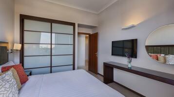 Une chambre d’hôtel avec un grand lit, un téléviseur fixé au mur, un bureau en bois et une porte coulissante donnant sur une autre pièce.