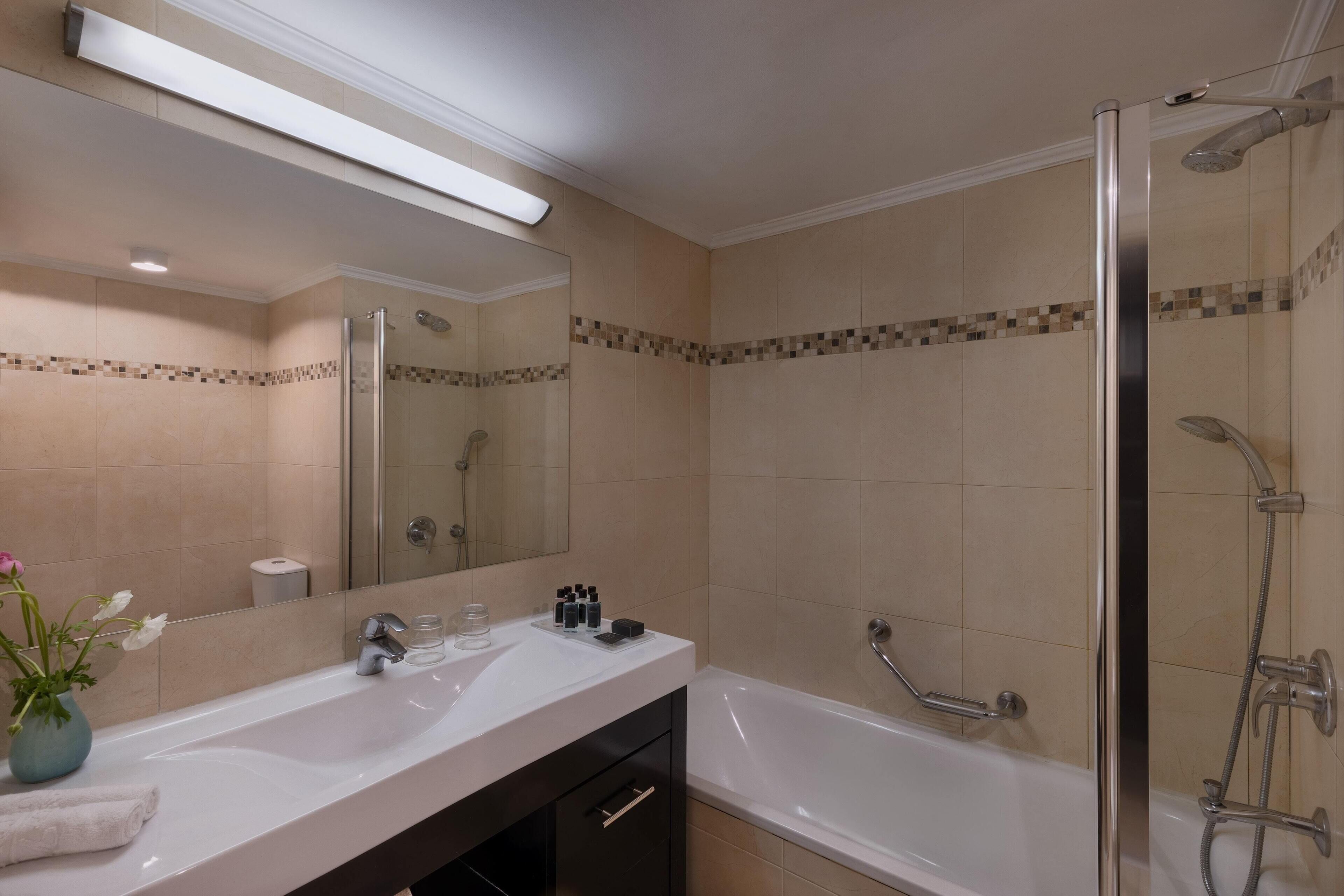 A modern bathroom with a large mirror, a white sink, a bathtub, and a shower area.