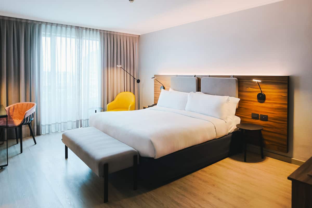 Una habitación de hotel moderna con una cama grande, una mesita de noche, una silla y un escritorio.