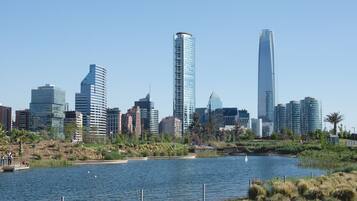 A city skyline with modern skyscrapers, a body of water, and a park area with people.