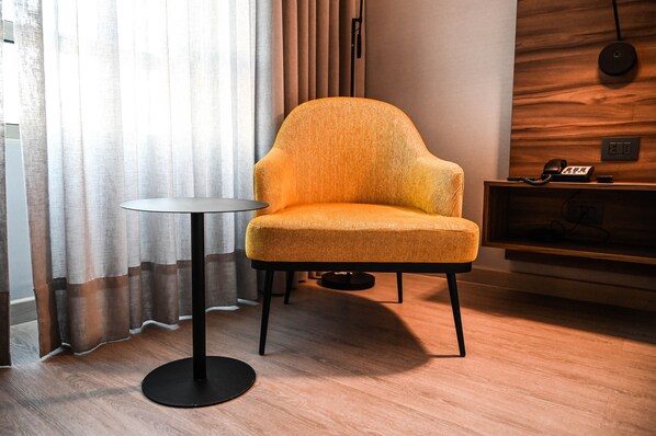 Una habitación moderna con un sillón amarillo, una mesita redonda, un panel de pared de madera y un teléfono en un estante de madera.