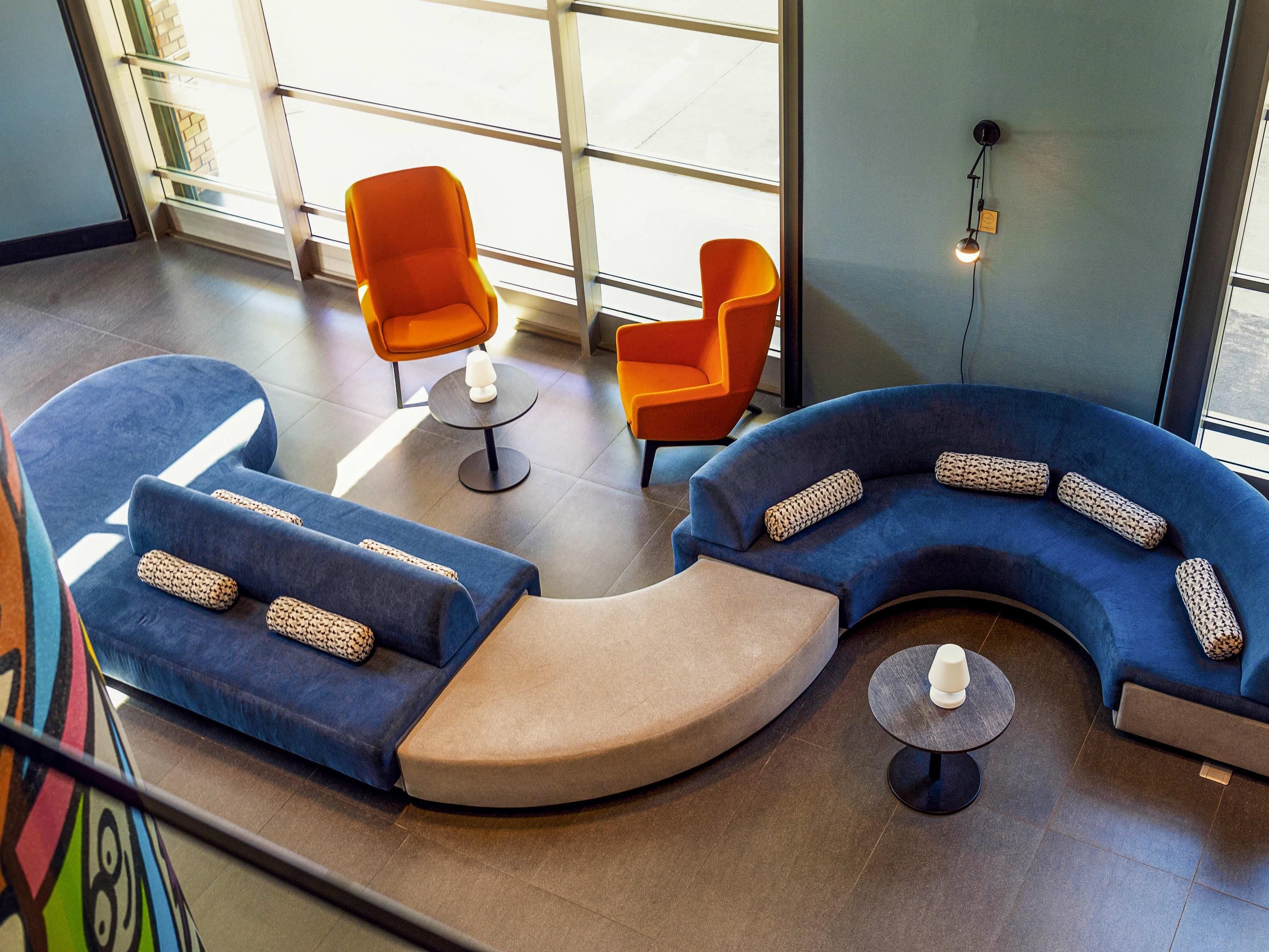 A modern lounge area with blue and orange seating, a small table, and a wall-mounted light fixture.