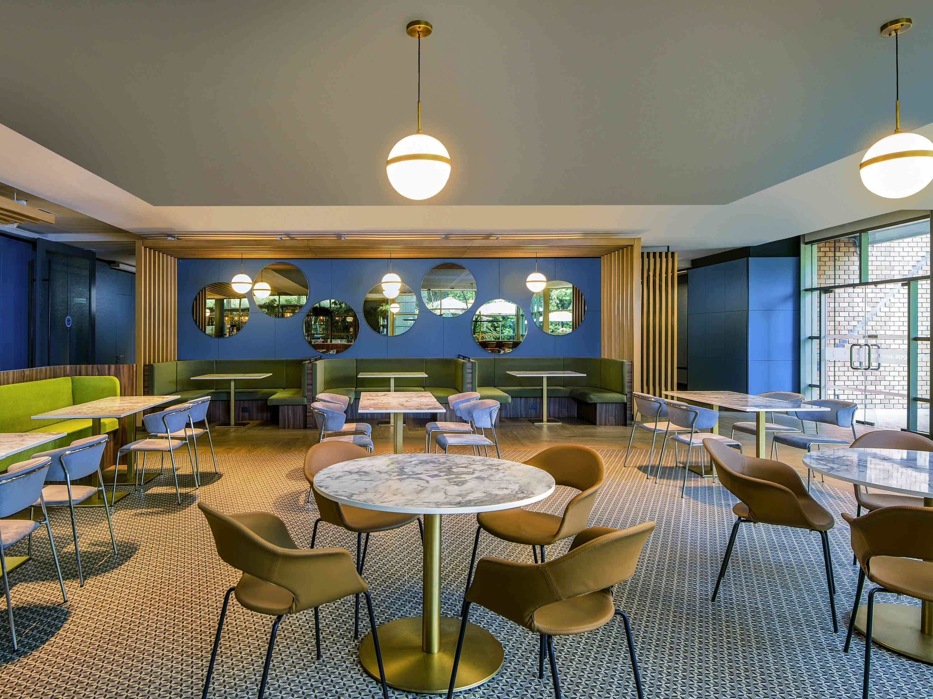 A modern restaurant interior with round tables, green booths, and mirrored wall decorations.