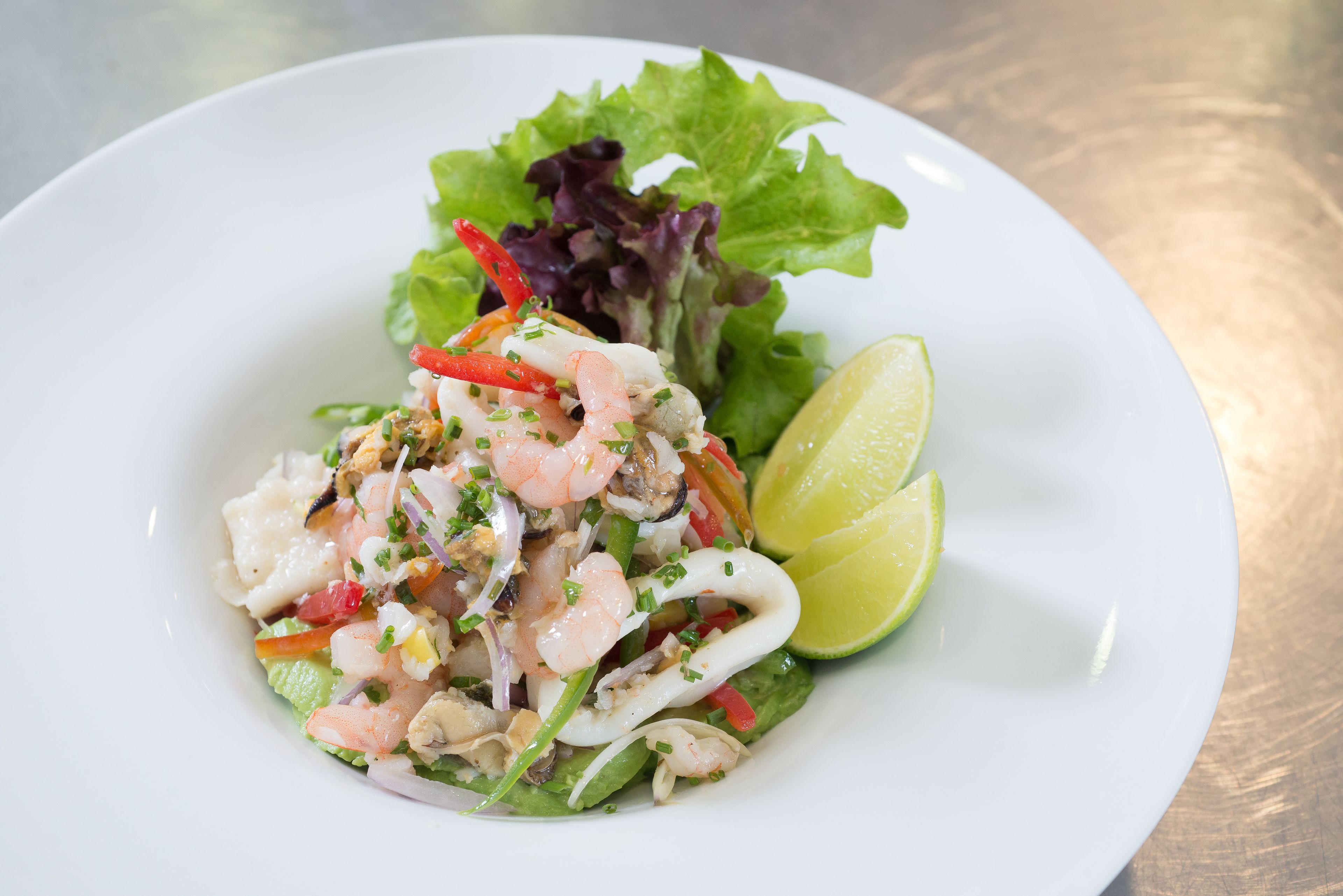 Ensalada de mariscos con camarones, calamares y verduras, servida en un plato blanco con una rodaja de limón.