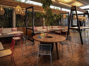 An indoor seating area with a round wooden table, red and black chairs, and a sofa with cushions. - Novotel Santiago Las Condes (Santiago)