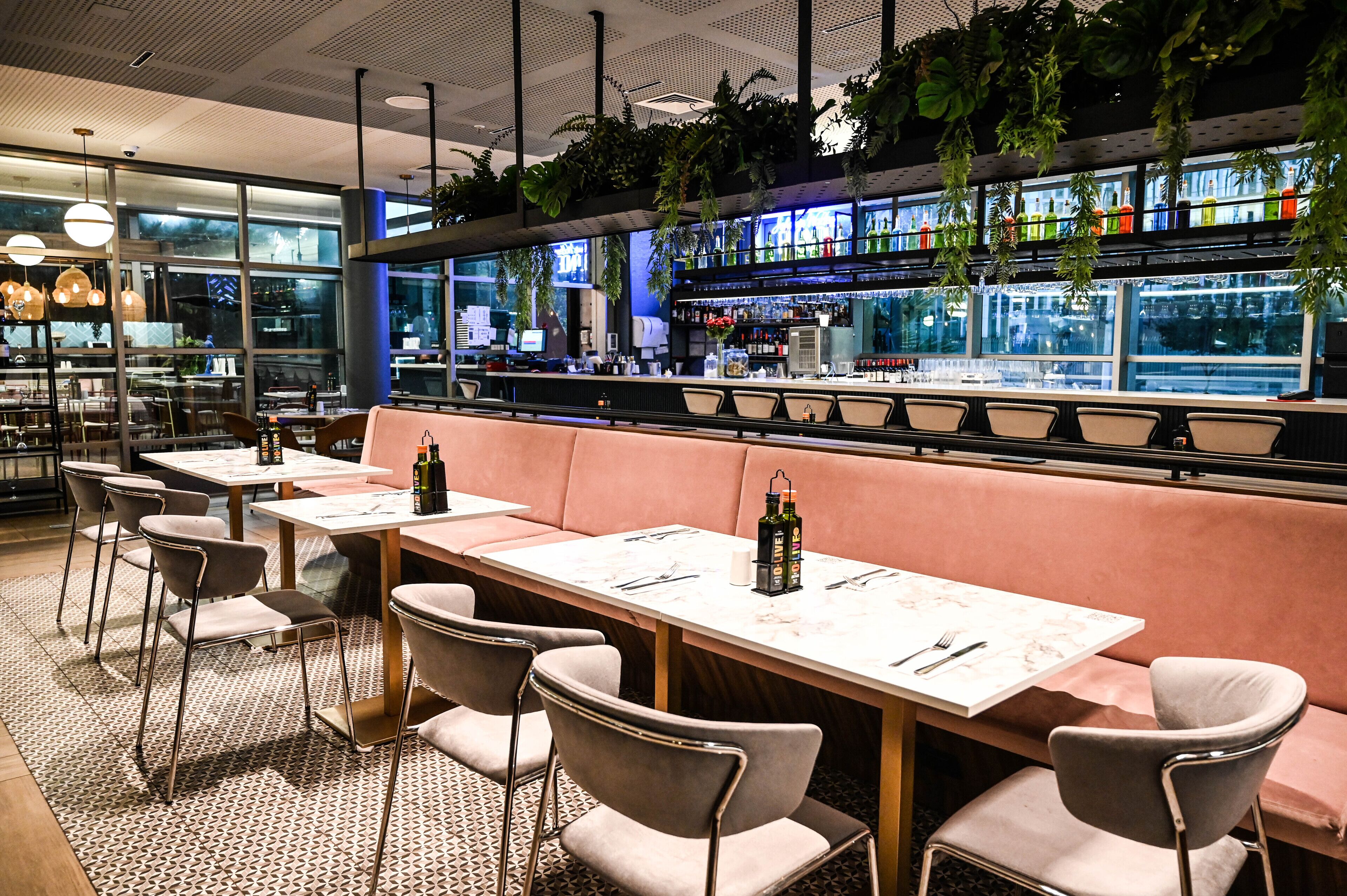 Un restaurante con mesas y sillas, una zona de bar y plantas colgantes.