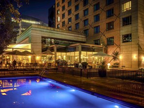 A hotel with a glass-enclosed outdoor area, a swimming pool, and a brick building facade. - Novotel Santiago Las Condes (Santiago)