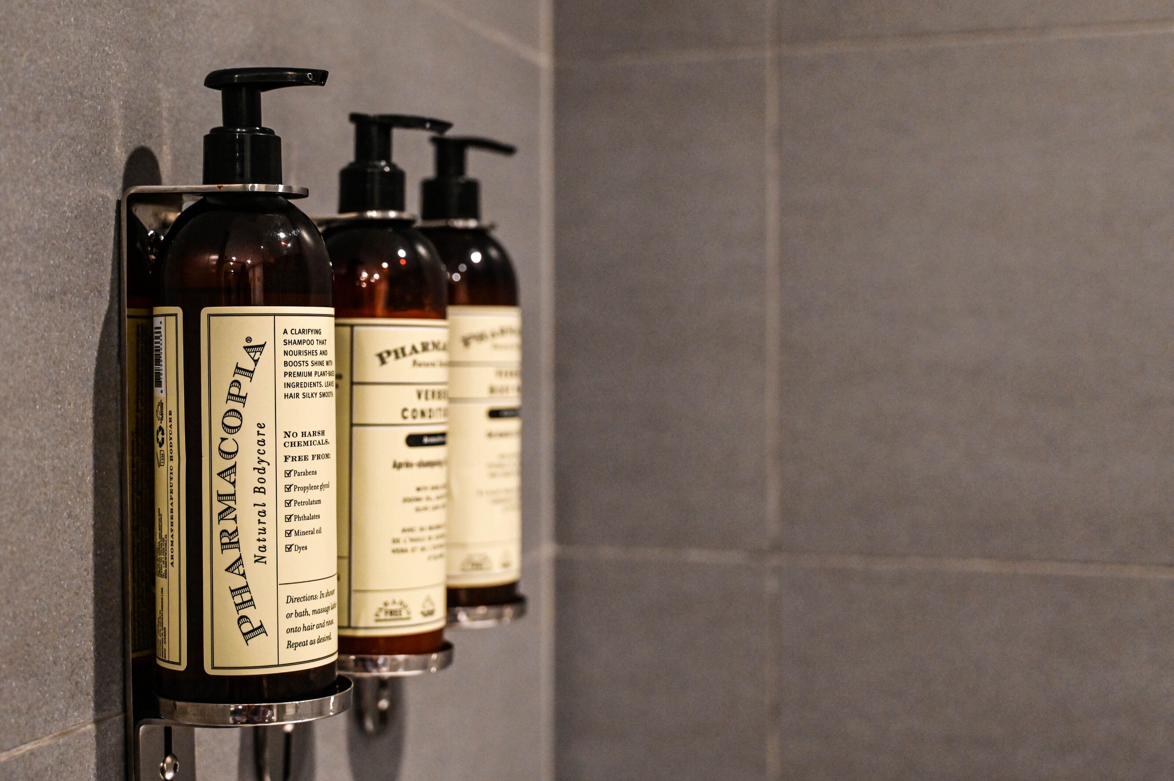 Tres botellas de productos de cuidado corporal PHARMACOPIA sobre una pared.