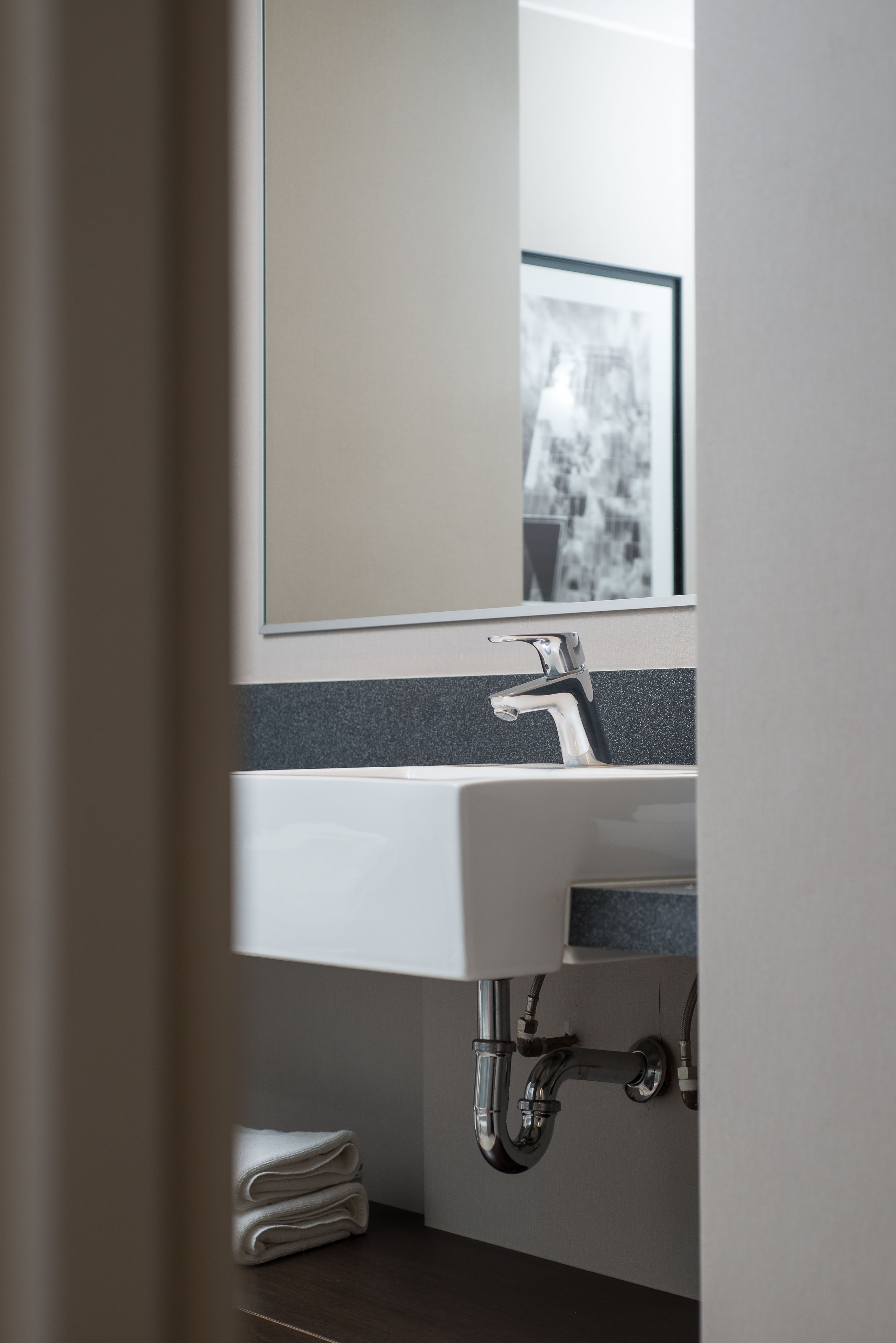 A modern bathroom with a white sink, chrome faucet, and a framed picture above the mirror.