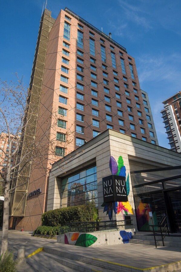 A modern hotel building with a prominent glass facade and a colorful logo on the entrance. - Novotel Santiago Las Condes (Santiago)