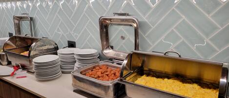 Montaje de bufé con diversos alimentos en recipientes metálicos, platos apilados y una pantalla digital de temperatura.