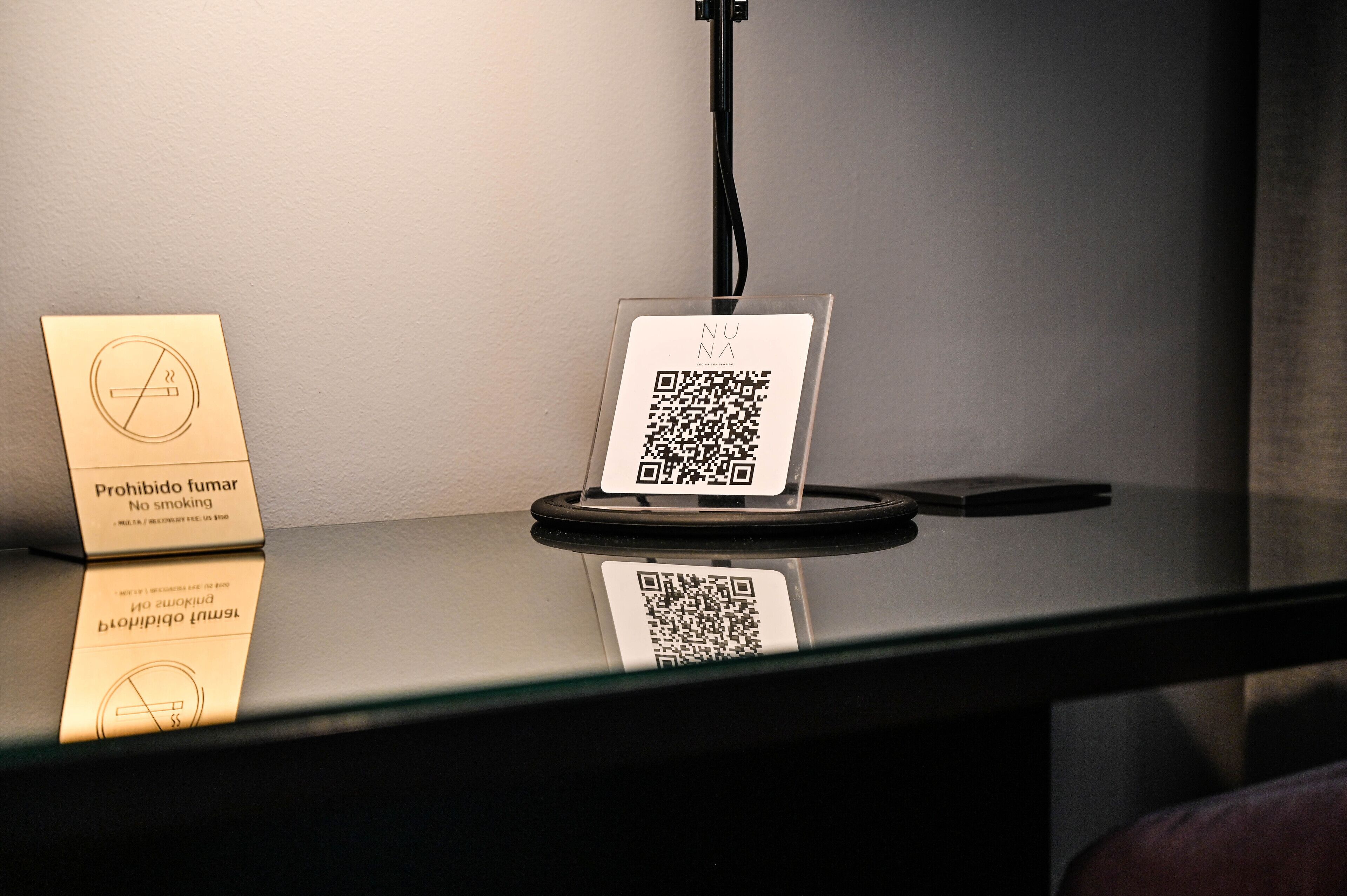 A table with a no-smoking sign and a QR code on a glass stand.