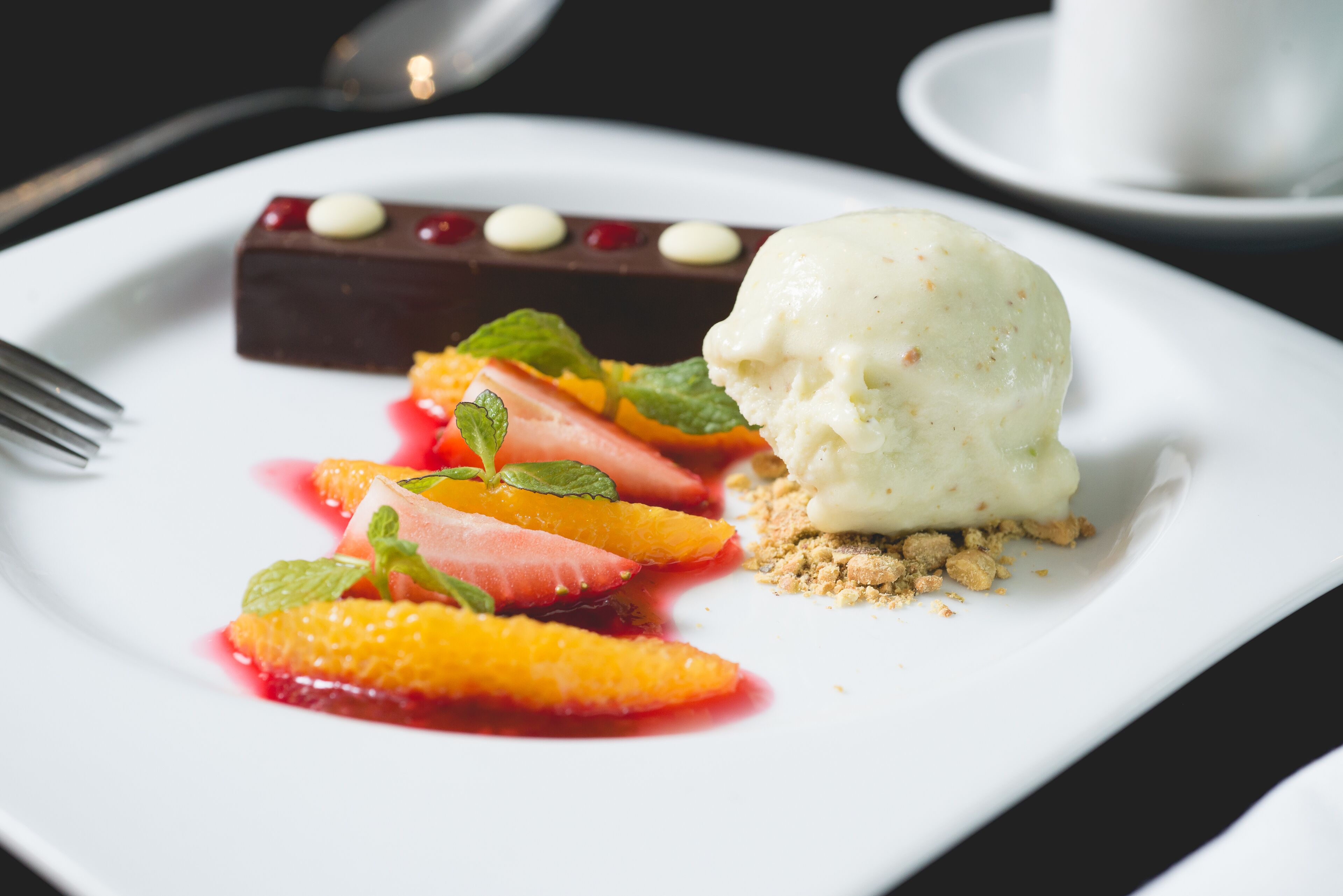 Un plato de postre con un trozo de chocolate, helado, fresas y rodajas de naranja.