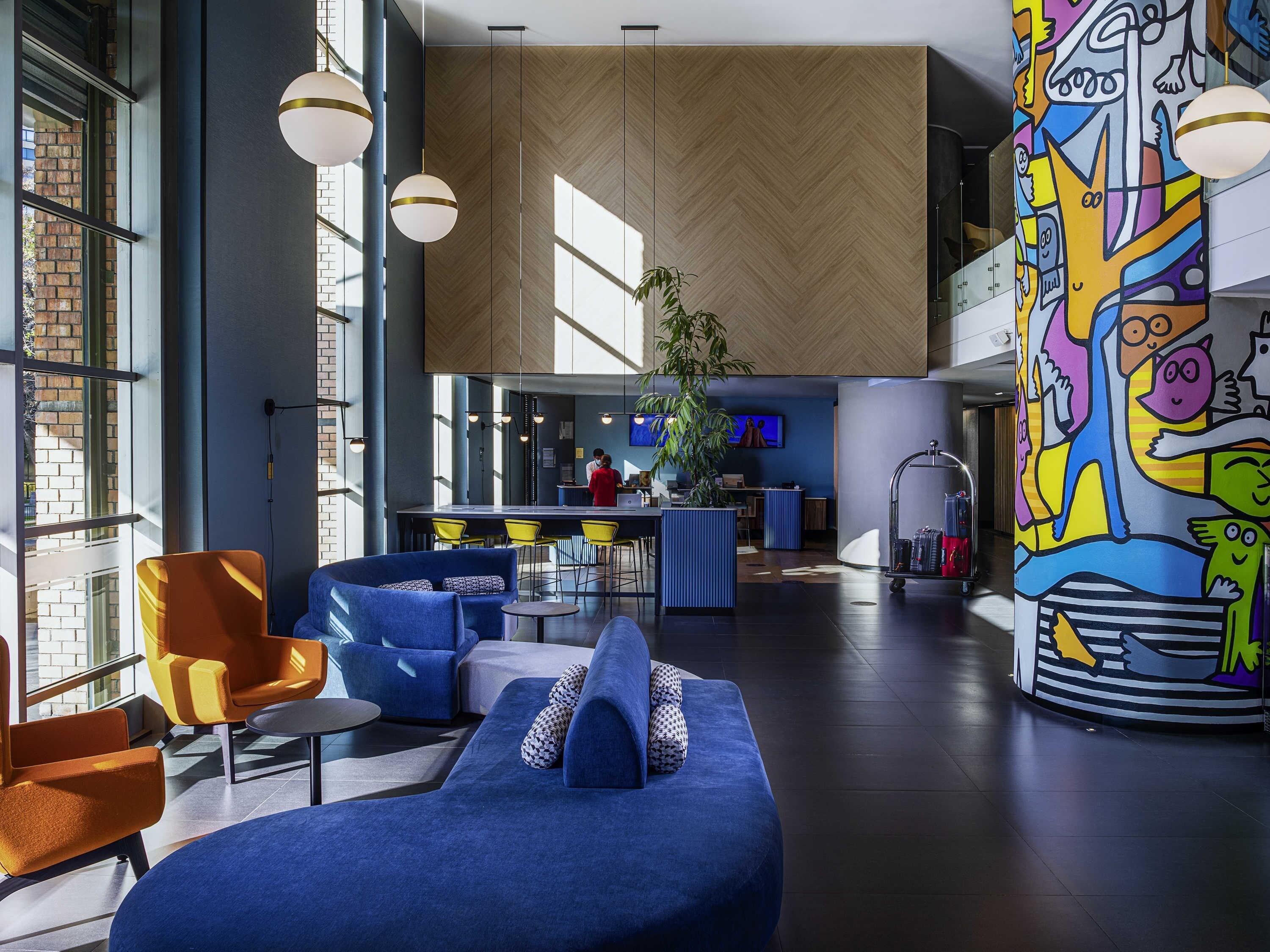 A modern lobby with a blue sofa, yellow chairs, and a colorful mural.