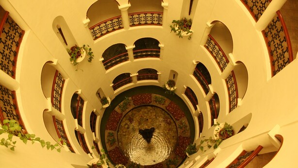 Un atrio de varios niveles con una fuente central, balcones con plantas y un suelo con diseño.