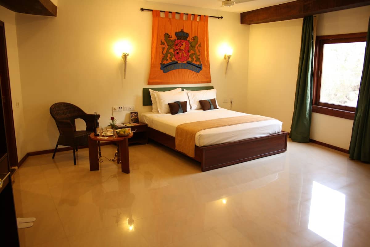A hotel room with a bed, a chair, a small table, and a window with curtains.