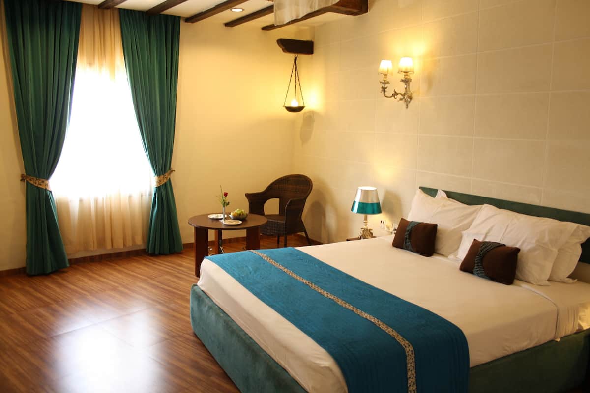 A hotel room with a large bed, a chair, a small table, and a wall-mounted lamp.