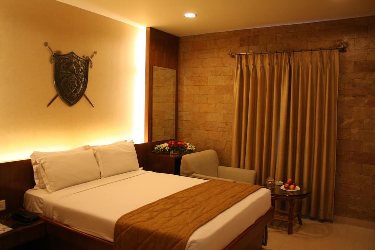 A hotel room with a bed, a nightstand, a chair, a table with fruit, and a curtain.