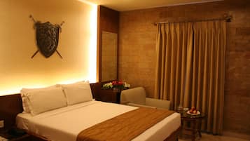 A hotel room with a bed, a nightstand, a chair, a table with fruit, and a curtain.