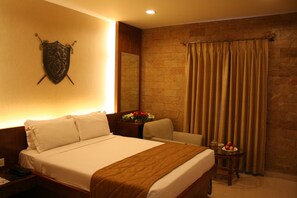A hotel room with a bed, a nightstand, a chair, a table with fruit, and a curtain. - Amrutha Castle (Hyderabad)