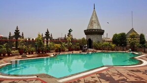 Una piscina con borde de baldosas, rodeada de plantas en macetas y elementos arquitectónicos.