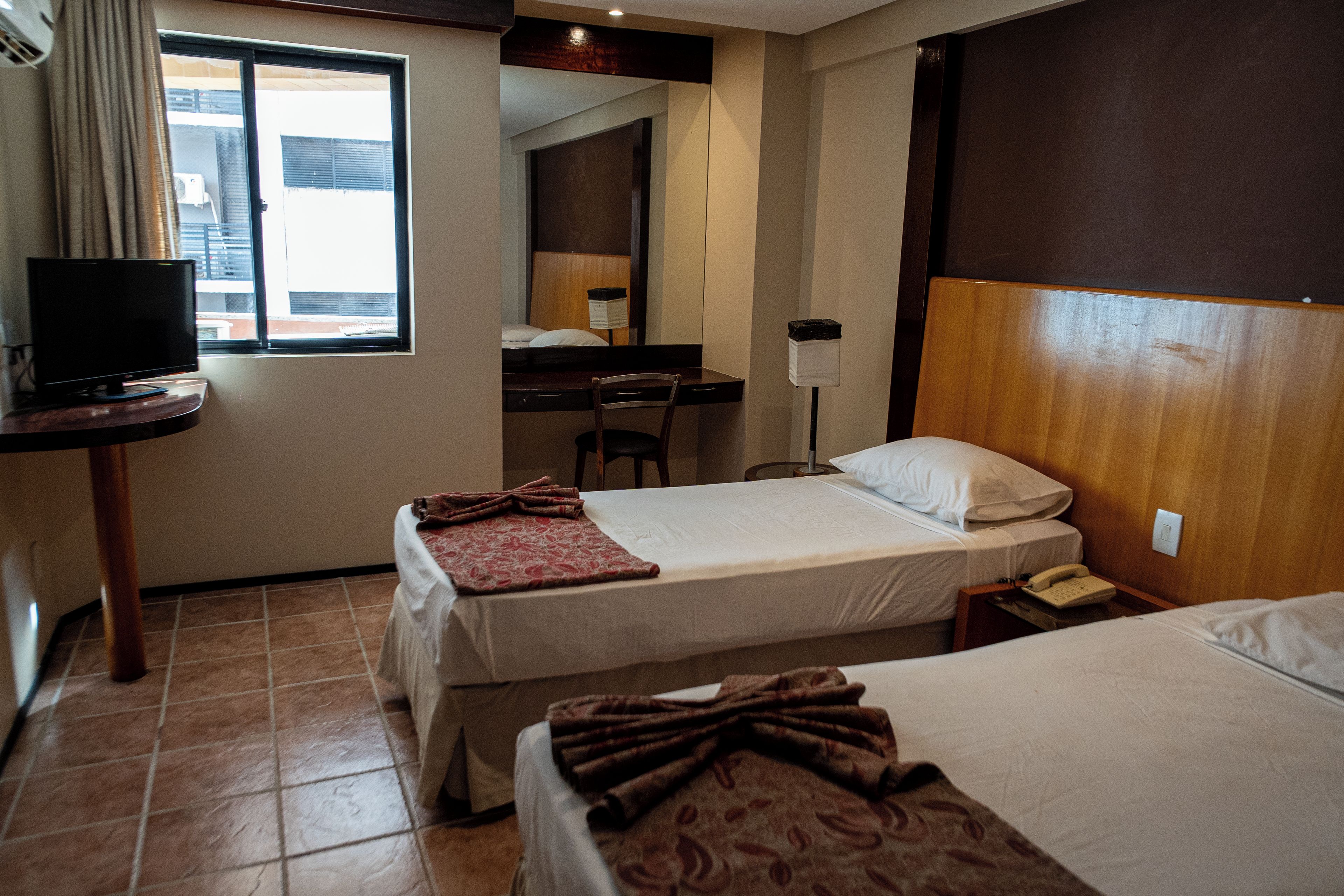 A hotel room with two beds, a desk, a chair, a television, and a window.