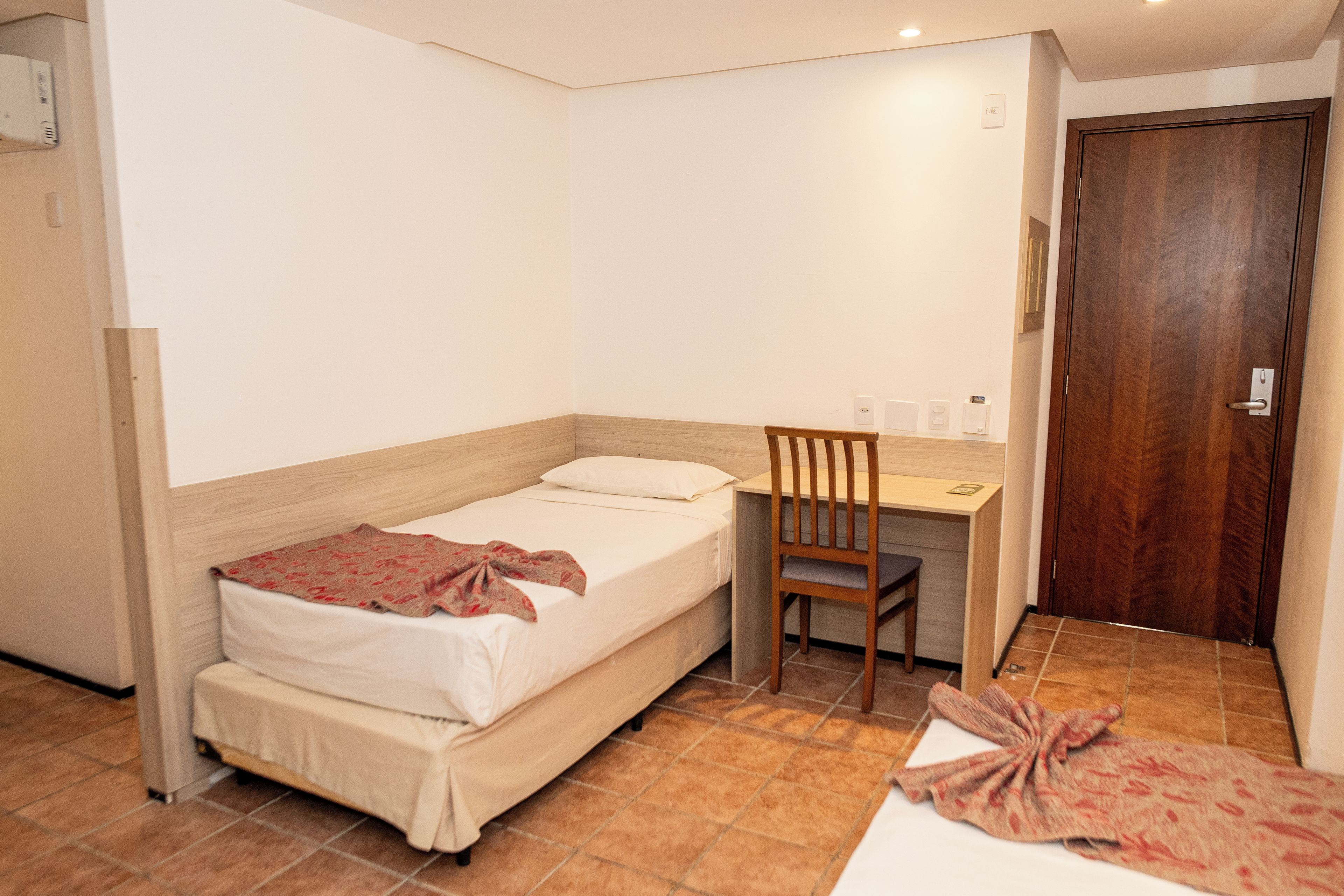 A small, neatly arranged bedroom with a single bed, a desk, and a chair.