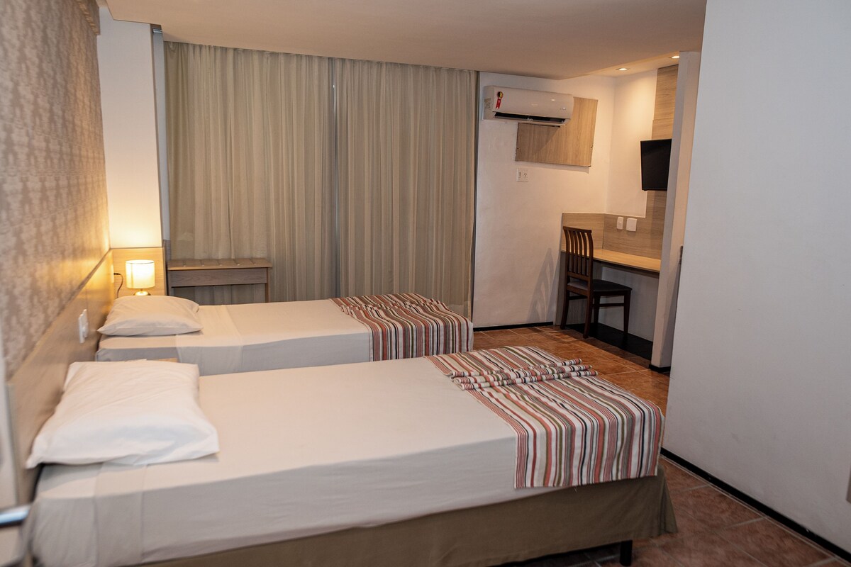 A hotel room with two beds, a desk, a chair, and an air conditioning unit.