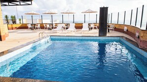 A swimming pool with lounge chairs and umbrellas, surrounded by a tiled deck. - Plaza Praia Suites (Fortaleza)