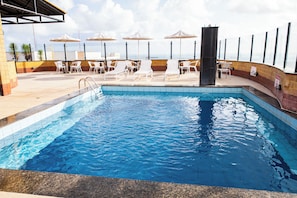 A swimming pool with lounge chairs and umbrellas, surrounded by a tiled deck. - Plaza Praia Suites (Fortaleza)